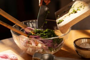 A Person Adding Chopped Green Leaves in a Bowl of Onion Slices